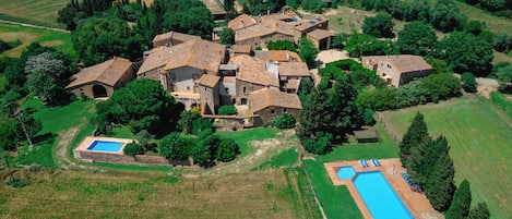 An aerial view of a rural estate with multiple stone buildings, a swimming pool, and surrounding greenery.