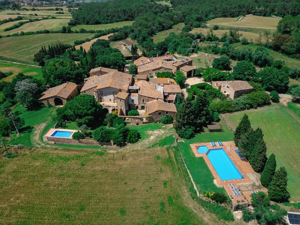 Vue aérienne d’un domaine rural comprenant plusieurs bâtiments en pierre, une piscine et une végétation luxuriante.