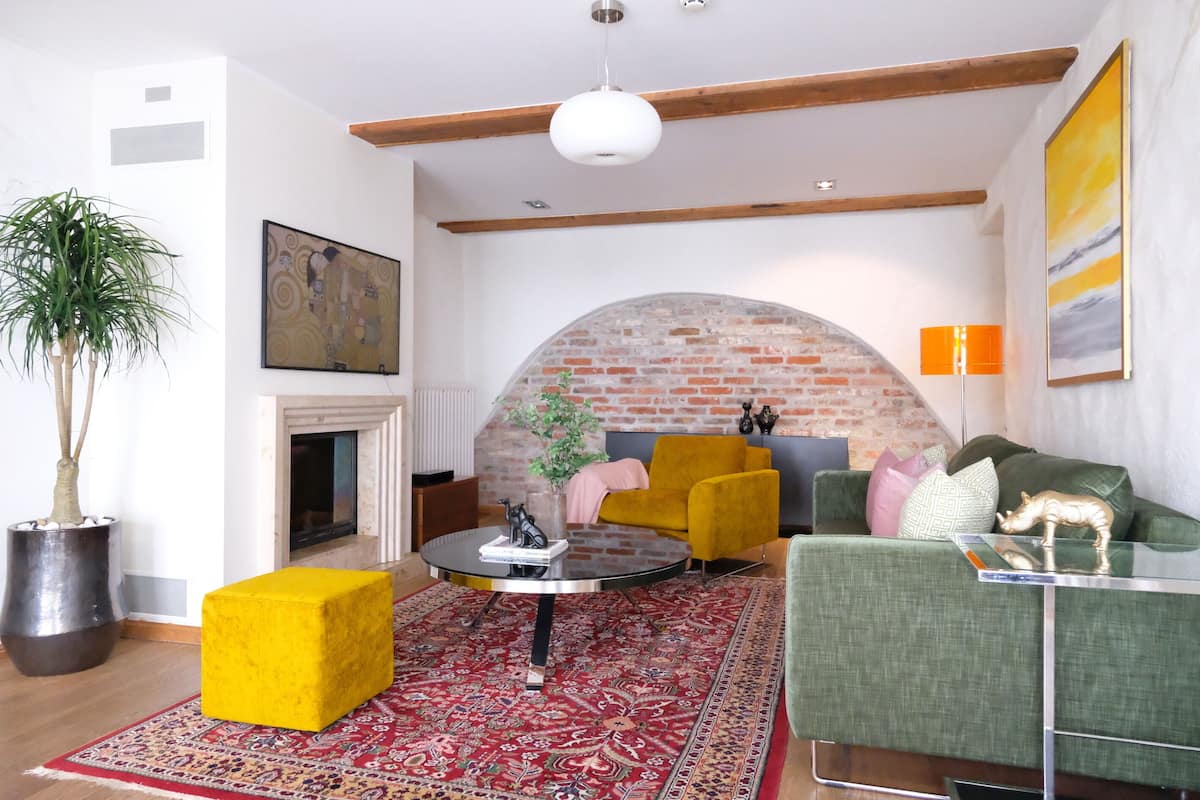Ein Wohnzimmer mit Kamin aus Ziegelsteinen, einem runden Couchtisch, einem gelben Sessel, einem grünen Sofa und einer großen Topfpflanze.