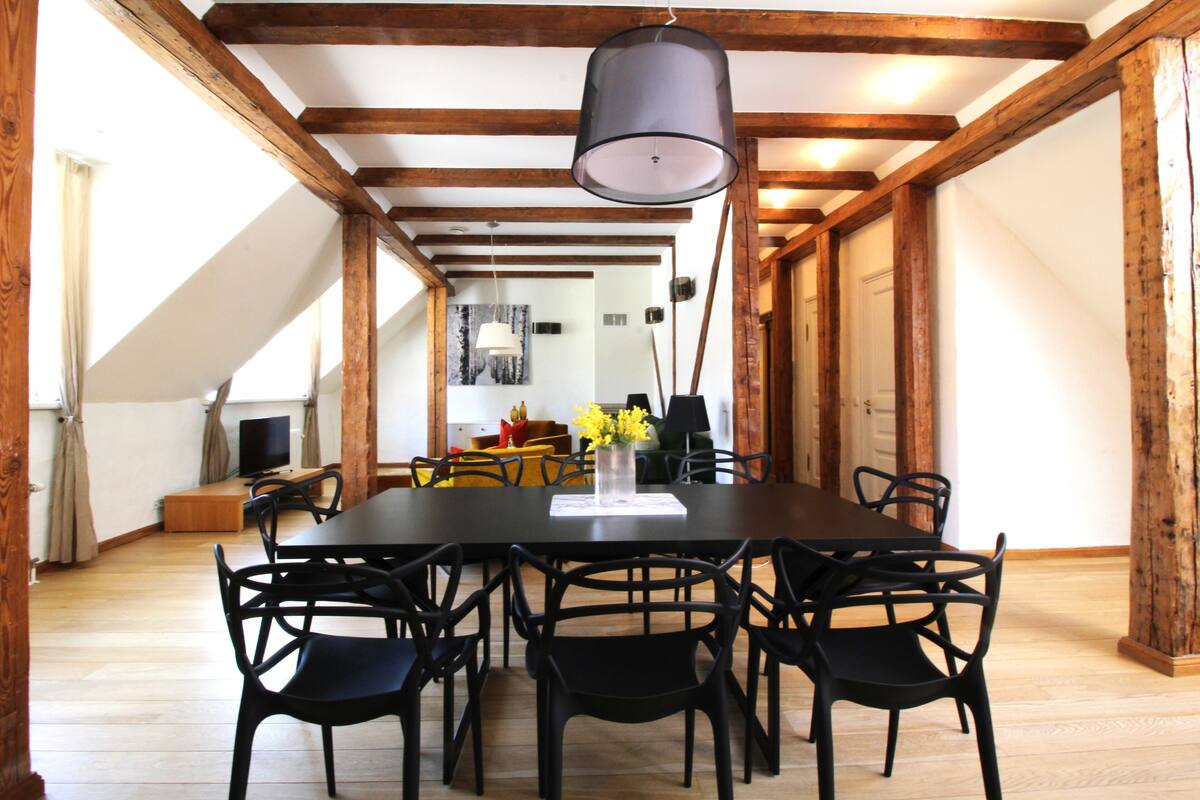Ein Essbereich mit großem Tisch und Stühlen, Holzbalken an der Decke und einem Fernseher im Hintergrund.