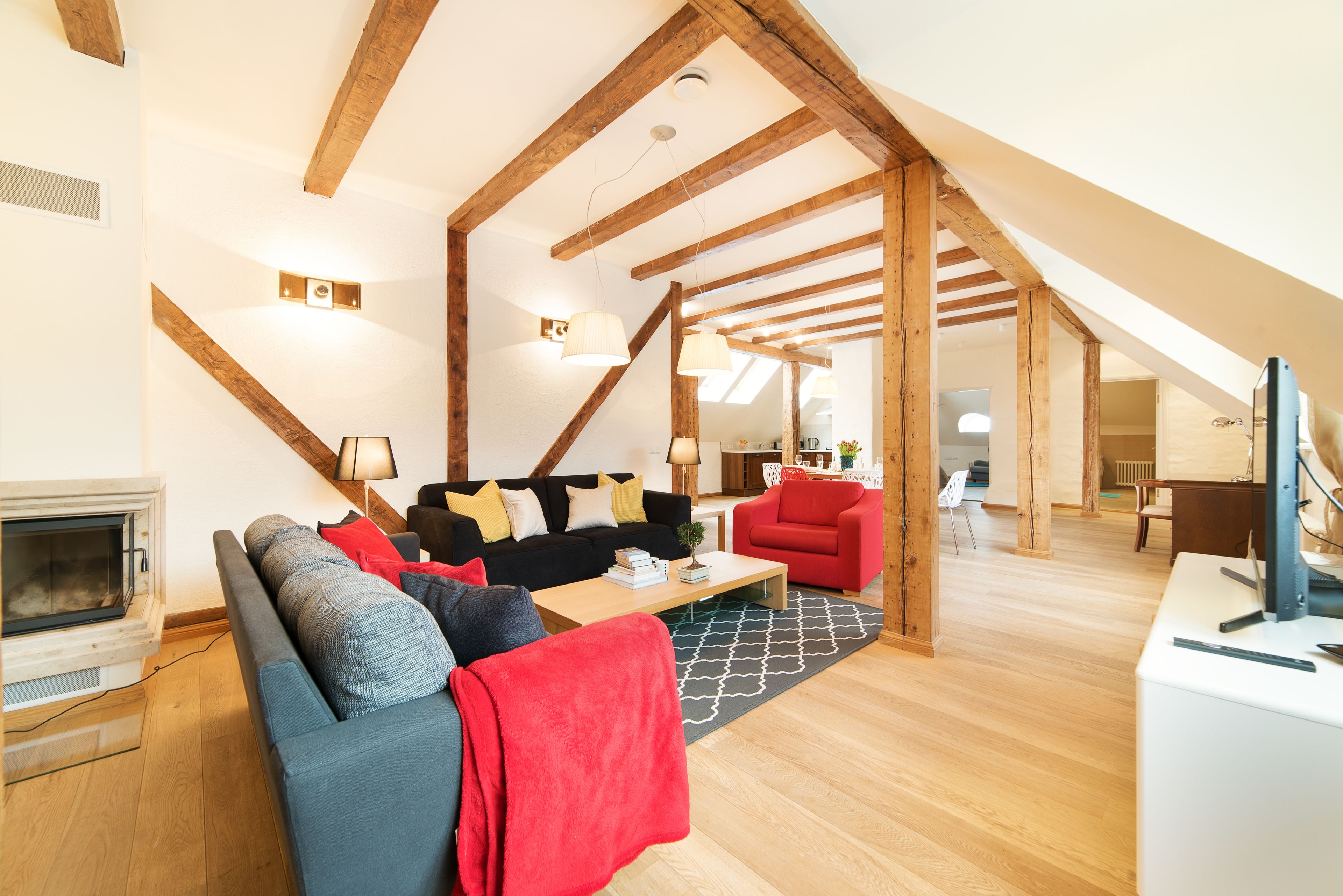 Un salon moderne avec une cheminée, un ensemble de canapés, un fauteuil rouge et une structure de plafond en bois.