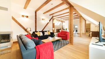 Un salon moderne avec une cheminée, un ensemble de canapés, un fauteuil rouge et une structure de plafond en bois.