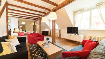 Ein geräumiges Wohnzimmer mit hohen Decken, Holzbalken, einem roten Sofa, einem schwarzen Sofa und einem Couchtisch aus Holz.