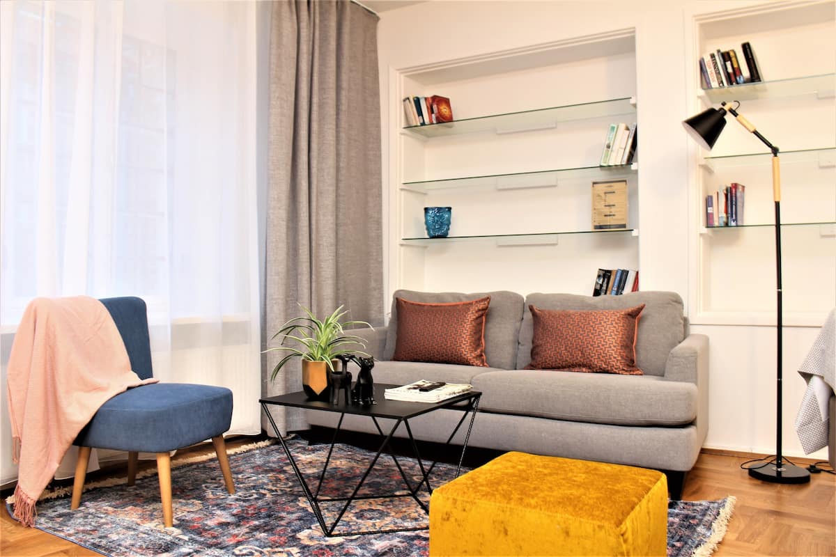Ein Wohnzimmer mit einer Couch, einem Couchtisch, einem Sessel, einem Bücherregal und einer Stehlampe.