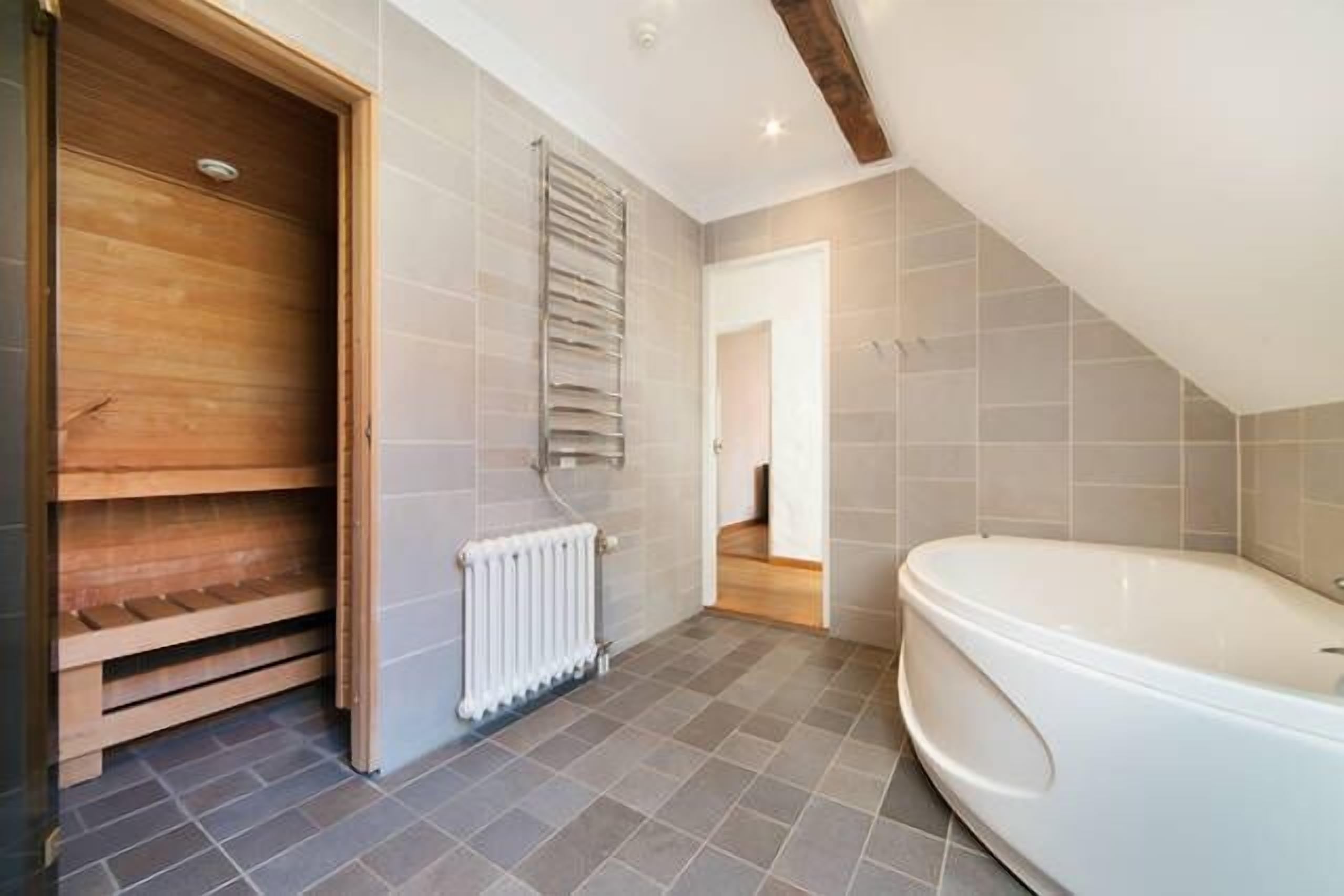 A modern bathroom with a bathtub, a wooden bench, and a radiator.