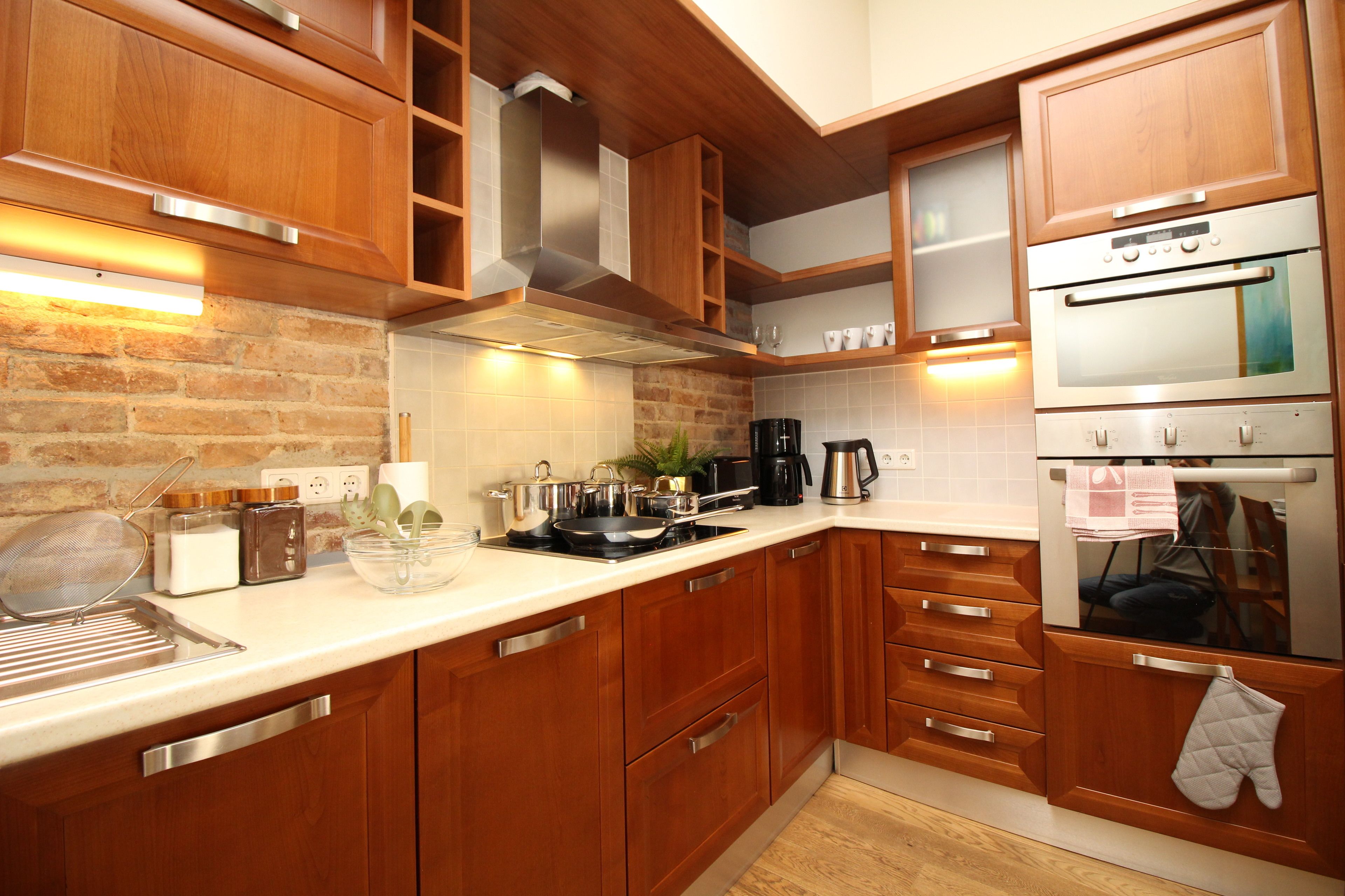 A modern kitchen with wooden cabinets, stainless steel appliances, and a brick wall.