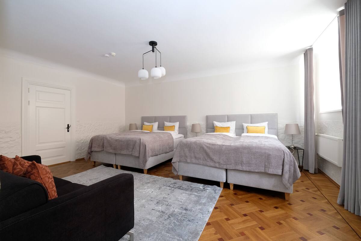 Ein modernes Hotelzimmer mit zwei Betten, einem Sofa und einem großen Fenster mit Vorhängen.