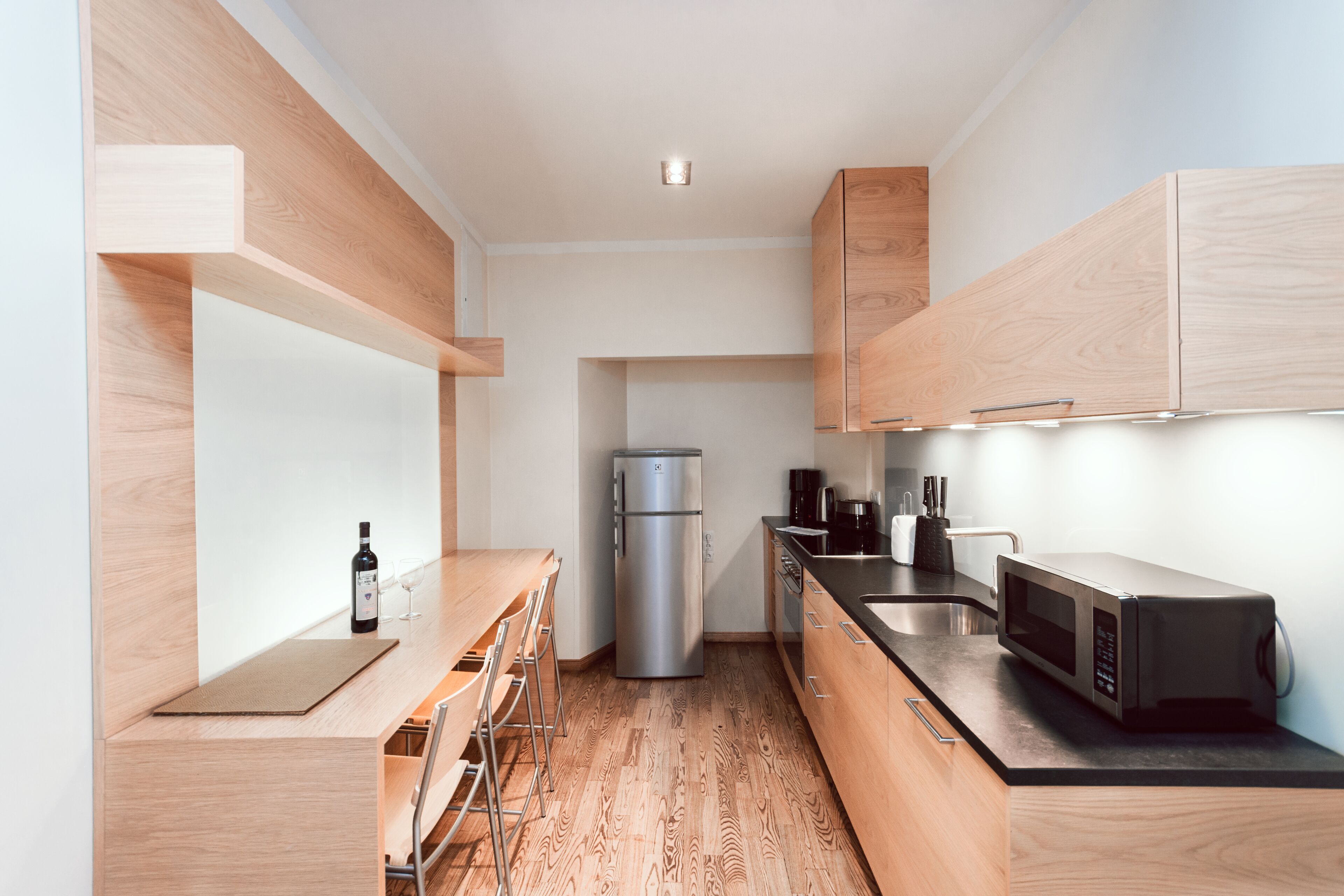 Una cocina moderna con armarios de madera, un refrigerador de acero inoxidable, un microondas y una mesa de comedor de madera con sillas.