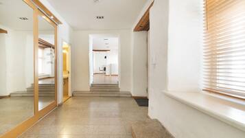 A hallway with a mirrored wall, a wooden floor, and a window with blinds.