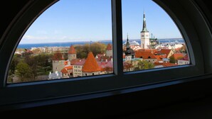 A view through a window of a historic town with a prominent church tower and a body of water in the distance. - Tallinn City Apartments Toompea Old Town (Tallinn)
