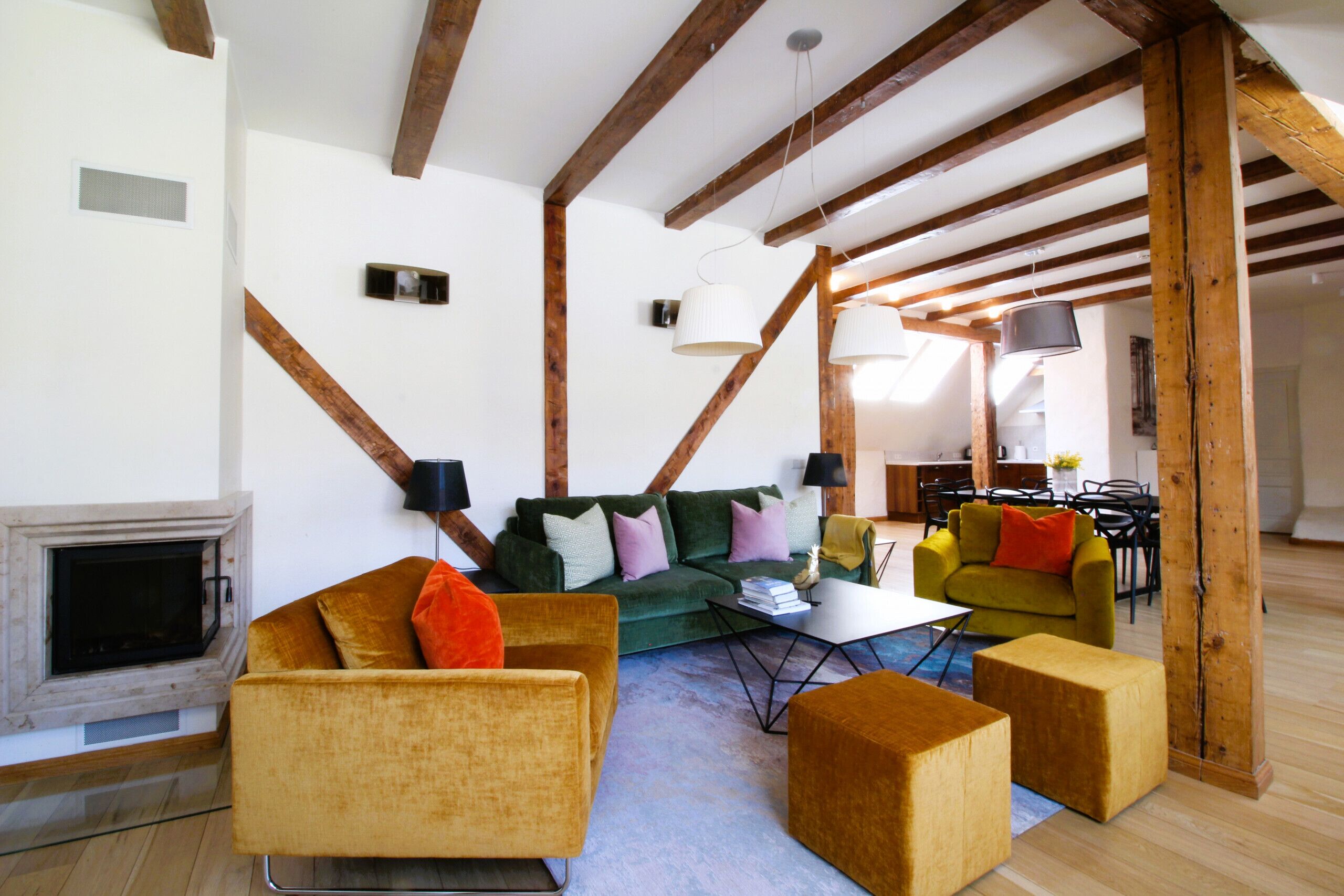 A living room with a fireplace, wooden beams, a green sofa, and a yellow armchair.