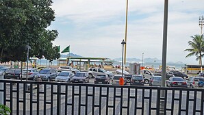 A busy parking lot with various cars and a bus, a green flag, and a building with a green roof in the background. - MZ Apartments Atlantica posto 6 (Rio de Janeiro)