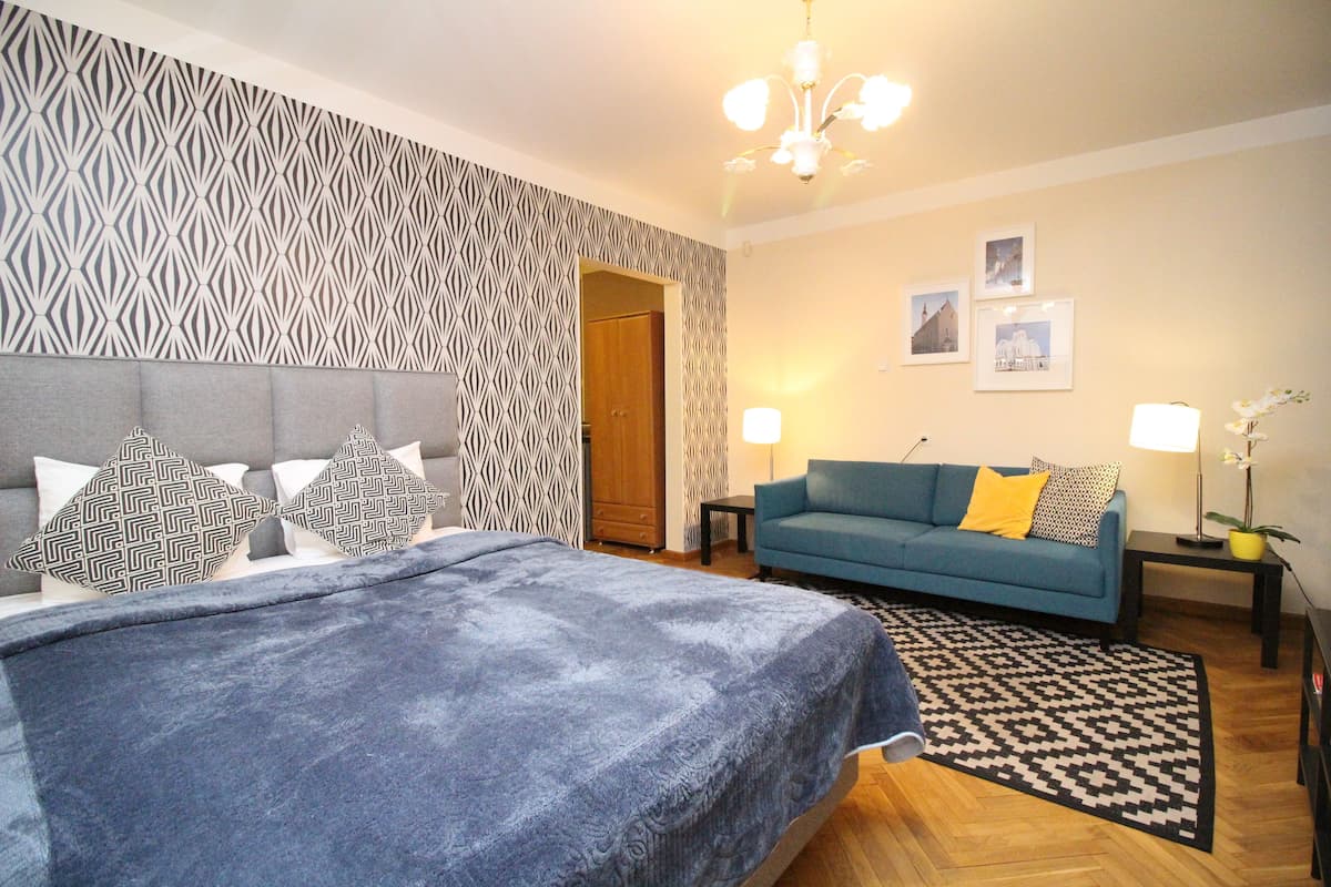 A bedroom with a bed, a blue sofa, a patterned wall, and a chandelier.