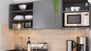 A modern kitchen with grey cabinets, a stainless steel refrigerator, a microwave, a coffee maker, and a wine bottle.