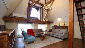 A loft-style living room with exposed wooden beams, a chandelier, a sofa, a coffee table, and a red chair.