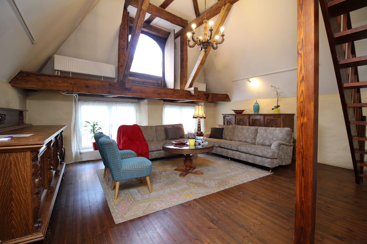 A loft-style living room with exposed wooden beams, a chandelier, a sofa, a coffee table, and a red chair.