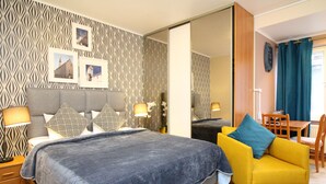 A bedroom with a bed, two nightstands, a sofa, a dining table, and a mirror.