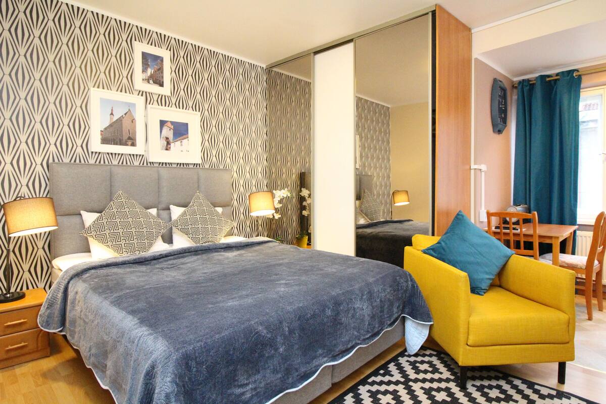 A bedroom with a bed, two nightstands, a sofa, a dining table, and a mirror.
