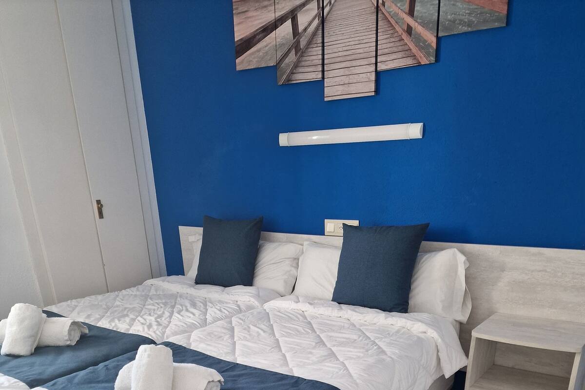 A neatly made bed with white and blue bedding, a wooden headboard, and a small bedside table.