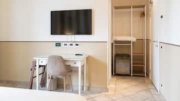 Une chambre d’hôtel comprenant un lit, un bureau avec une chaise, un téléviseur fixé au mur et un dressing avec des étagères.