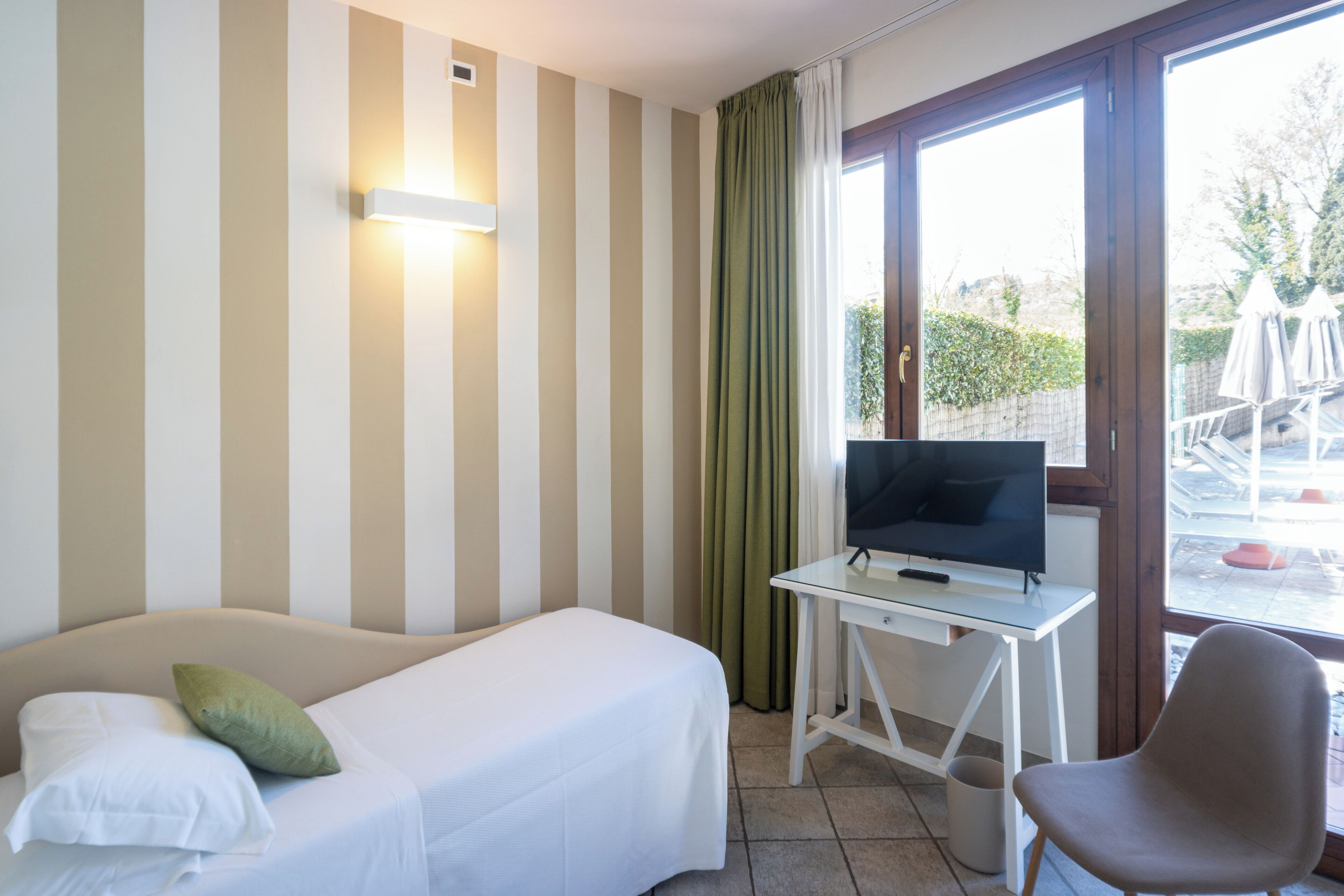 A hotel room with a bed, a desk with a TV, and a chair.
