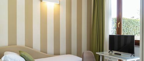 A hotel room with a bed, a desk with a TV, and a window with curtains.