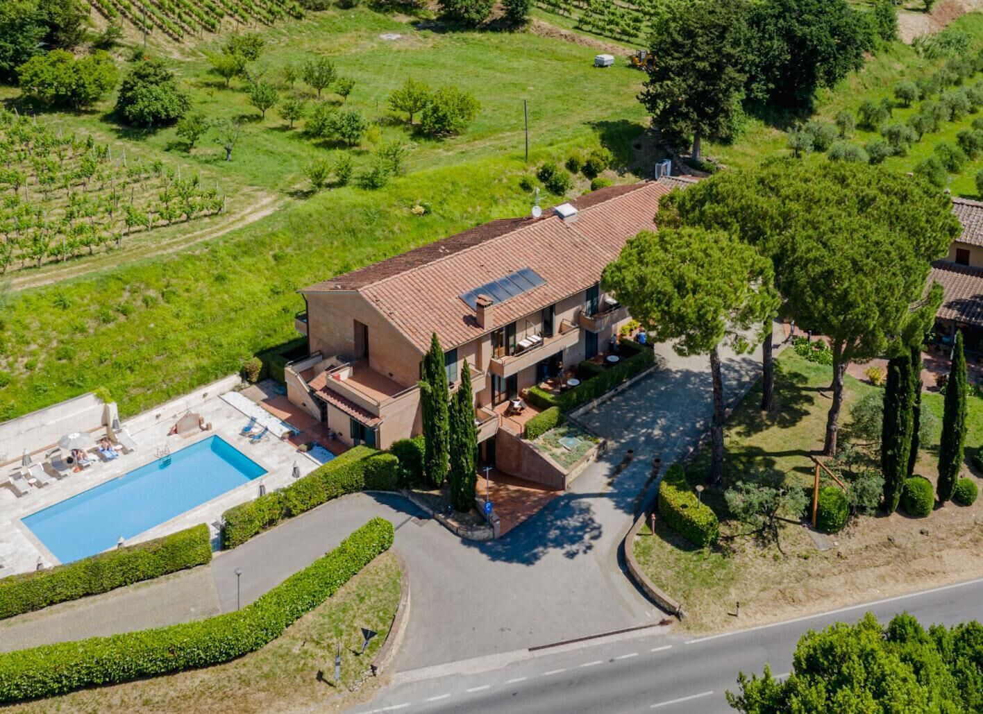 Una casa de dos pisos con piscina, rodeada de jardines cuidados y un viñedo.