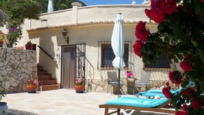 A villa with a stone wall, a tiled patio, a lounge area with a sunbed, and a table with chairs. - Villa Senomar (Benissa)
