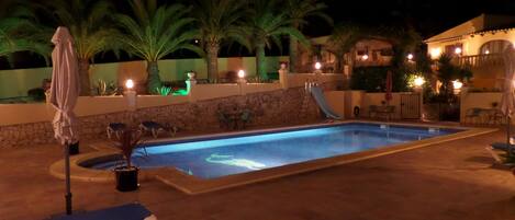 A swimming pool with lounge chairs, palm trees, and a stone wall.