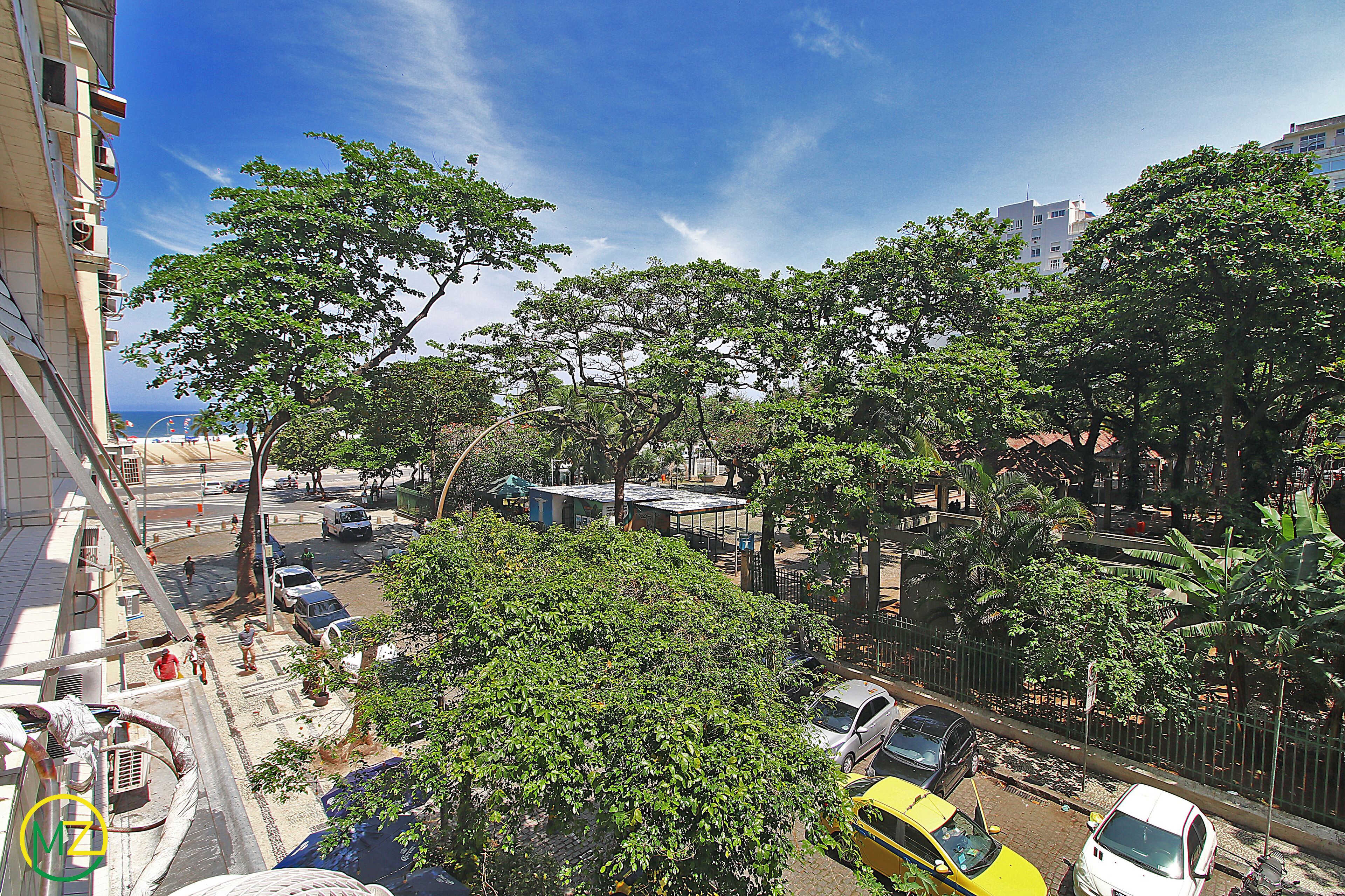 Vista de la calle con árboles, coches aparcados y edificios.