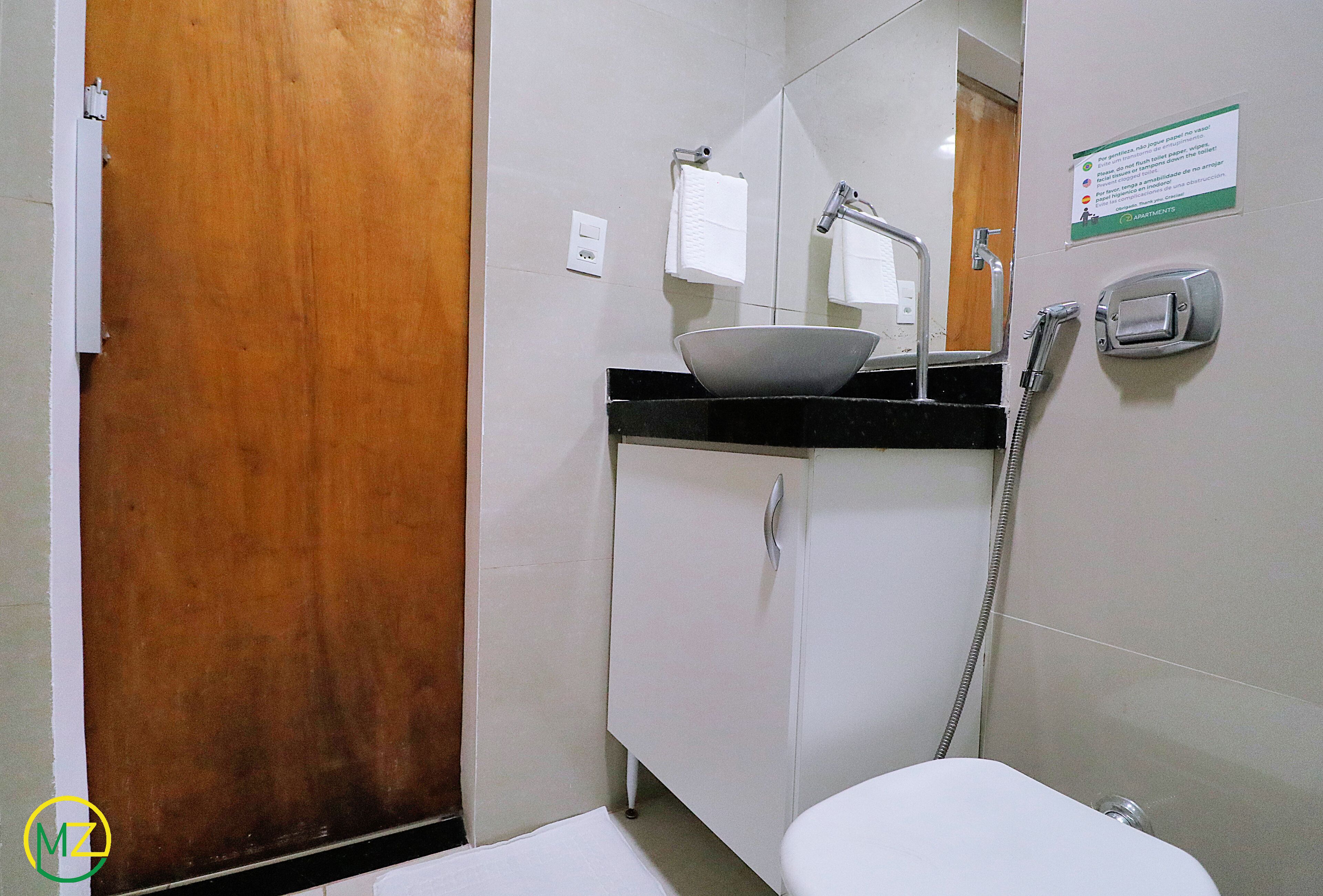 Un bagno con una porta in legno, un lavandino bianco con uno specchio grande sopra, un porta asciugamani e un telefono fissato al muro.