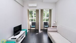 Un salon moderne avec un téléviseur à écran plat, deux fauteuils, un canapé et une fenêtre avec des rideaux.