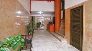Un couloir doté d’un sol en marbre, un comptoir d’accueil, des plantes en pot et une porte fermée.