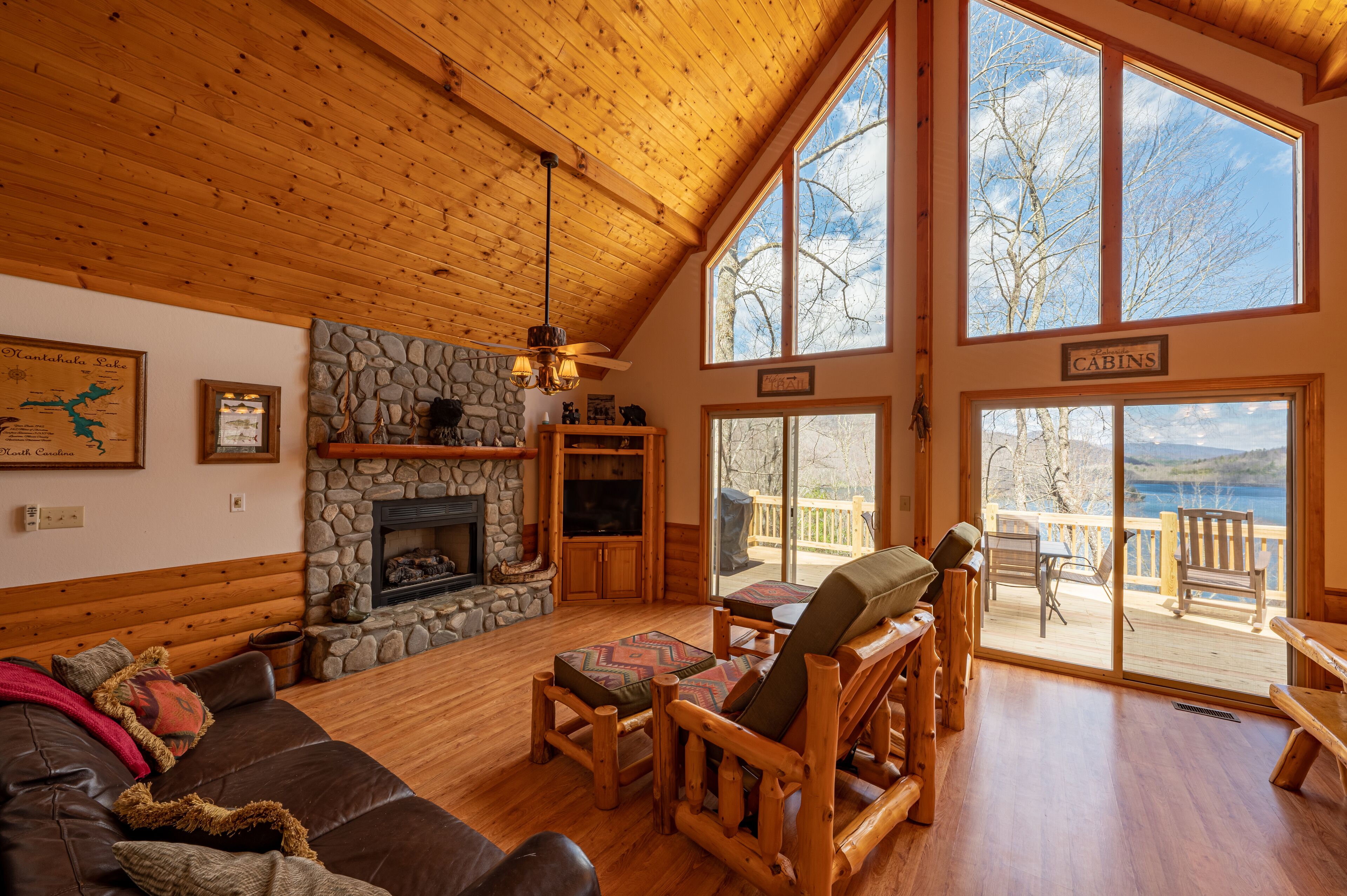 A spacious living room with a stone fireplace, wooden furniture, and large windows offering a view of the outdoors.