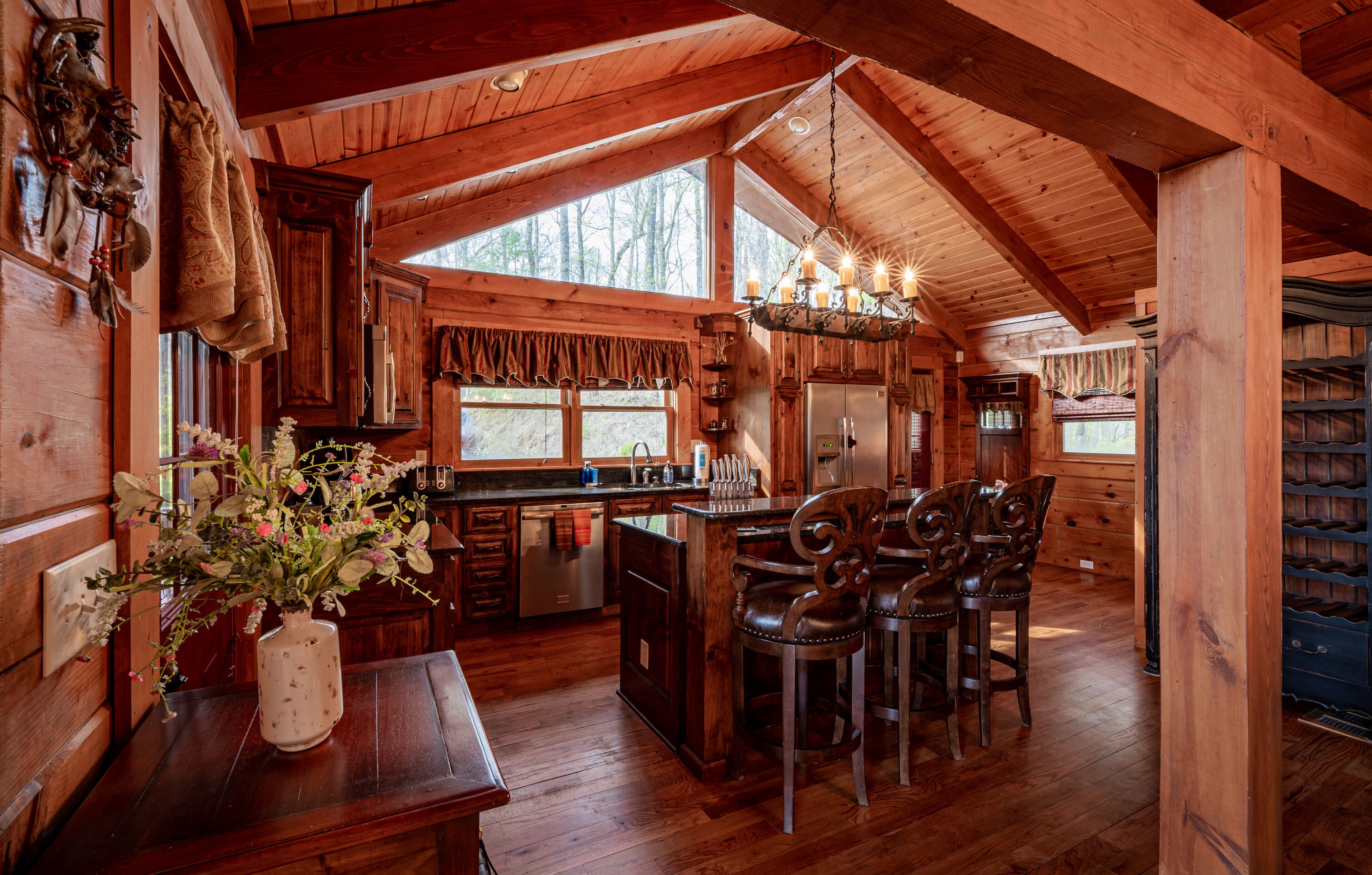 A rustic wooden cabin with a kitchen featuring a large island, bar stools, and a chandelier.