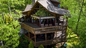A multi-level wooden cabin with a deck, surrounded by dense forest. - stayNantahala - Smoky Mountain Cabins (Topton)