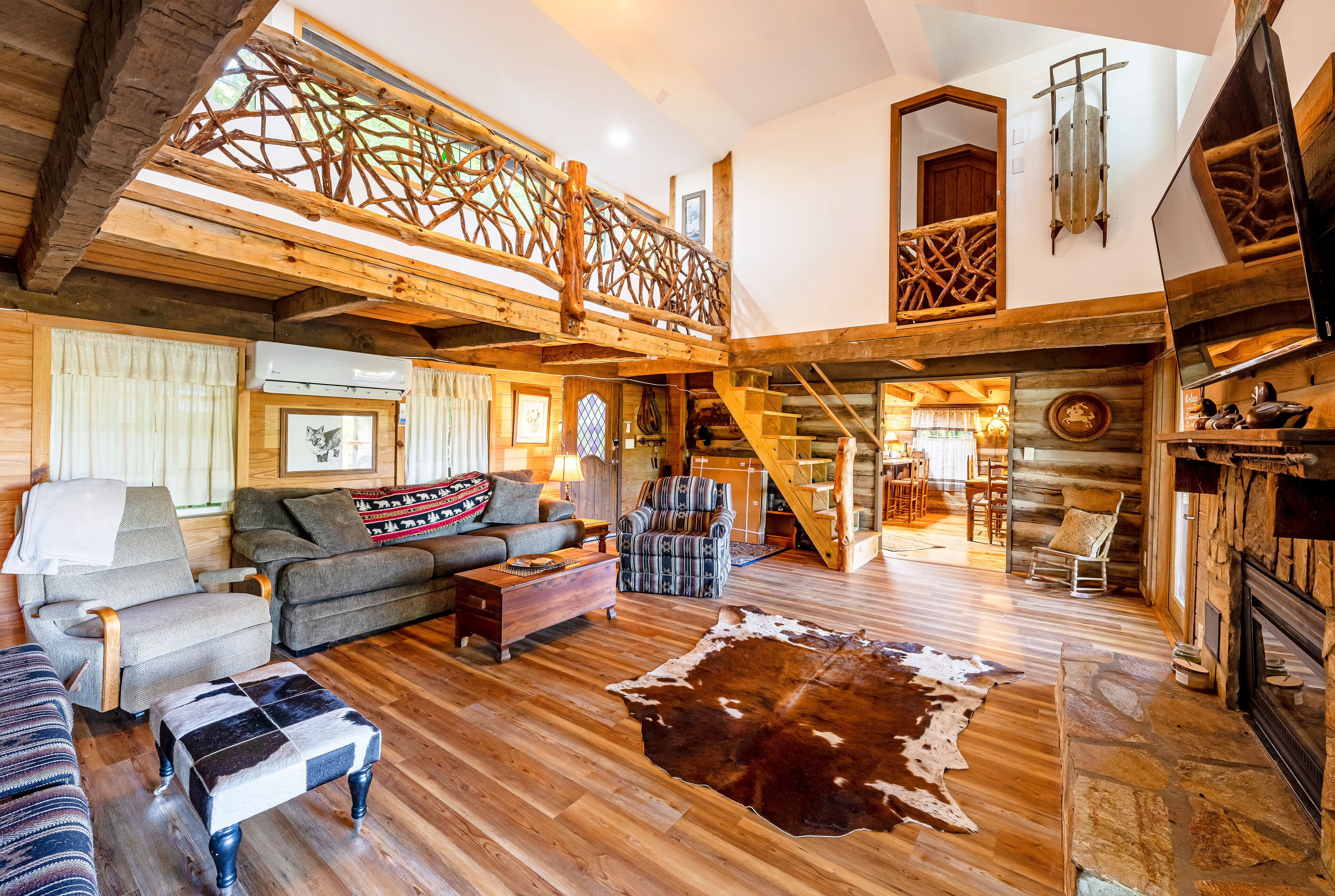 A spacious living room with wooden floors, a large leather rug, and a staircase leading to an upper level.