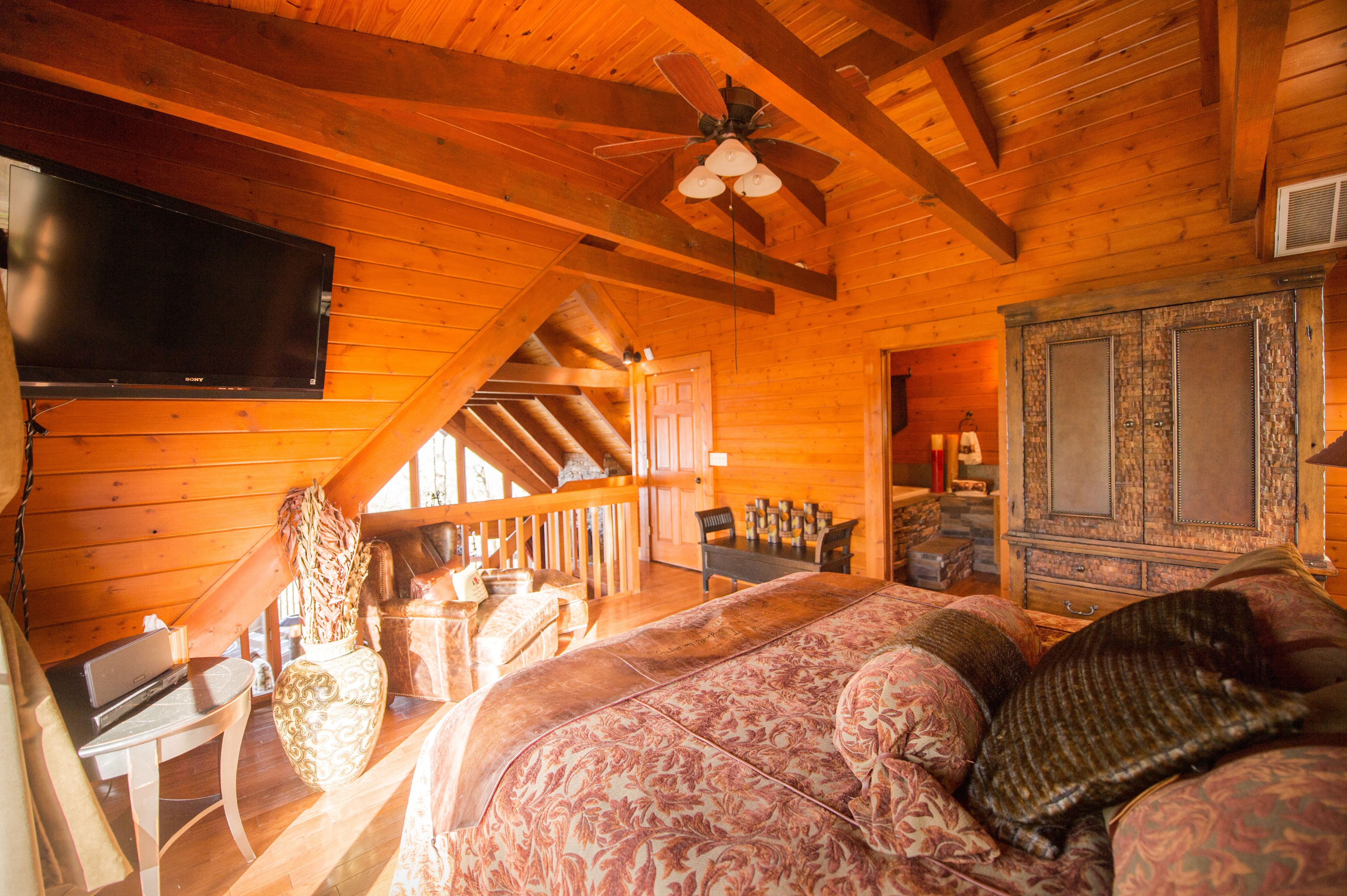 Ein gemütliches Schlafzimmer in einer Holzhütte mit einem großen Bett, einem Fernseher und einem Deckenventilator.