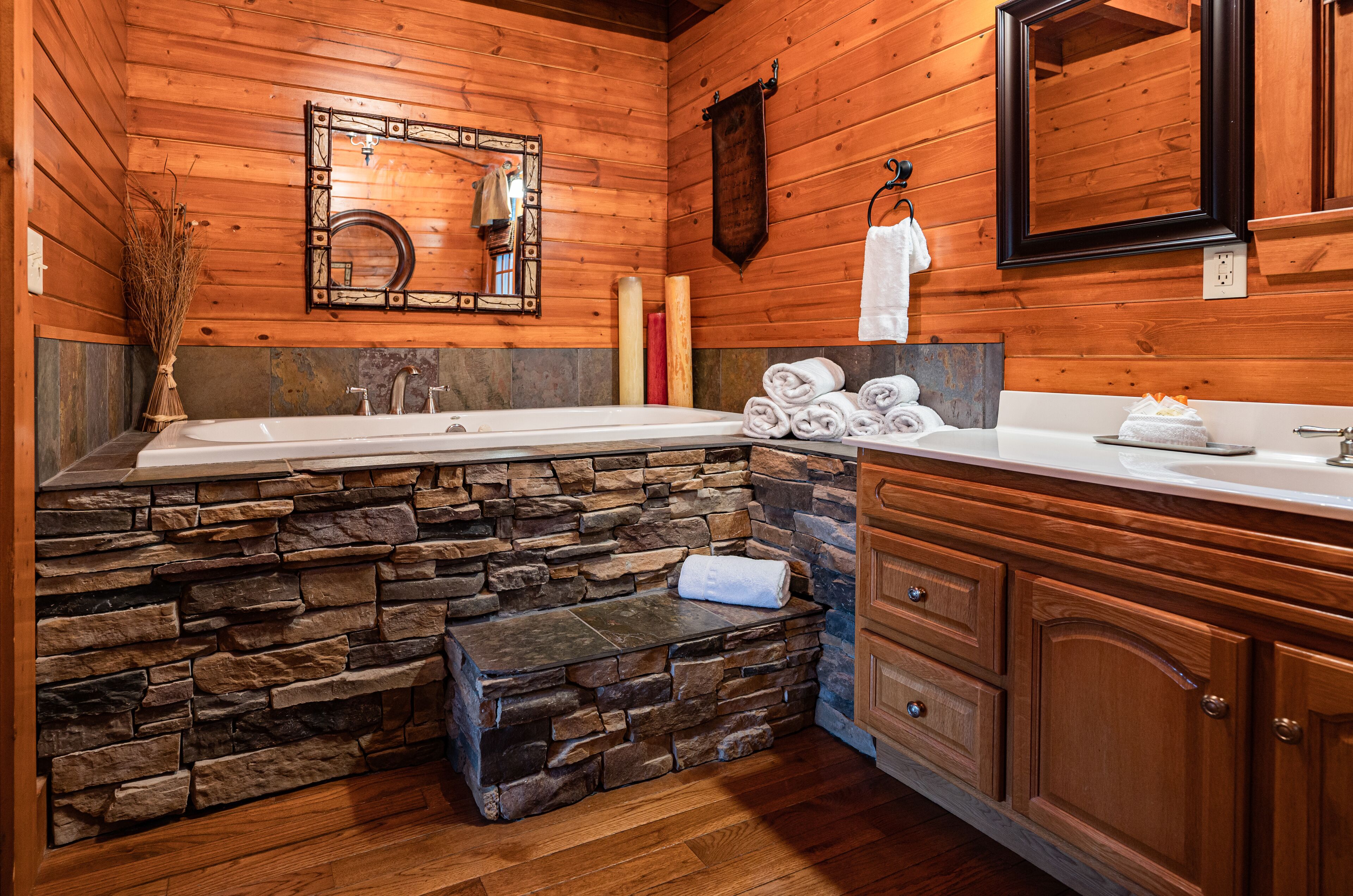 A bathroom with a stone wall, wooden cabinets, a large mirror, and a bathtub.