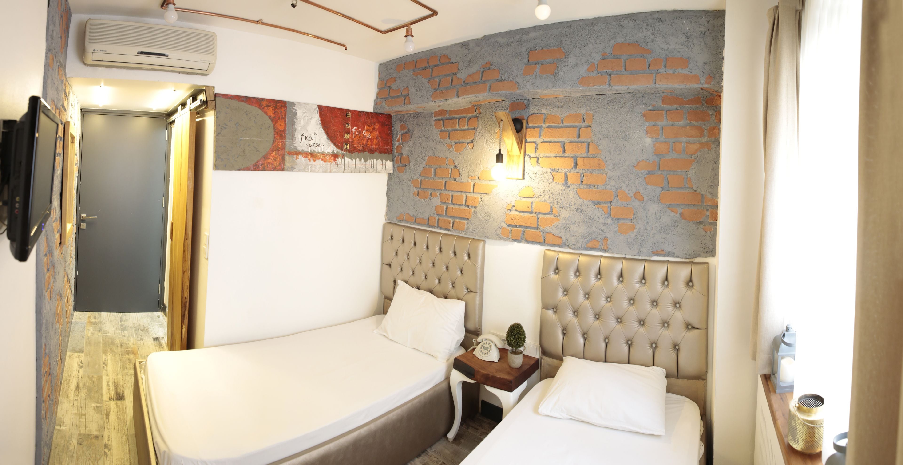 A bedroom with a brick wall, a bed, a nightstand, and a wall-mounted light.