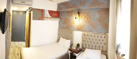 A bedroom with a brick wall, a bed, a nightstand, and a wall-mounted light.