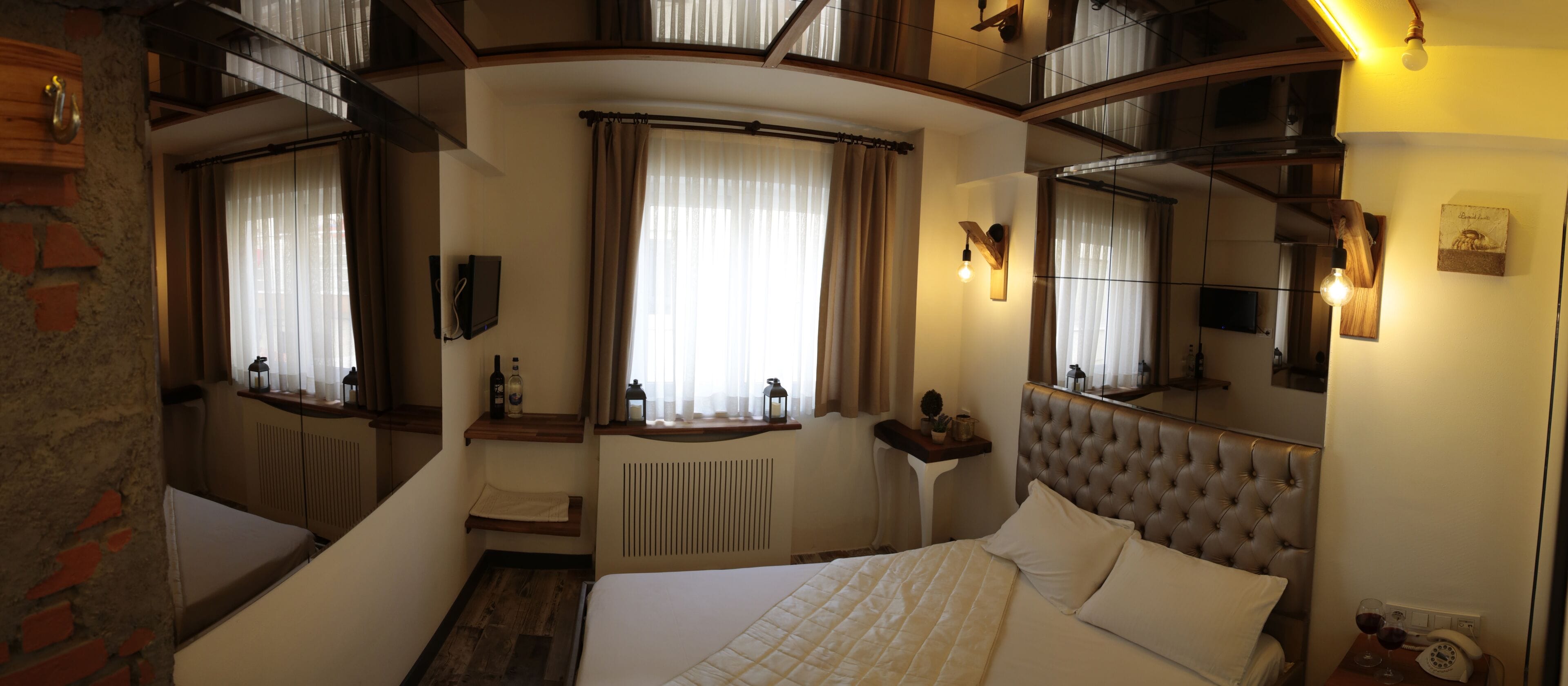 Una habitación de hotel con cama, mesita de noche, espejo, ventana con cortinas y radiador.