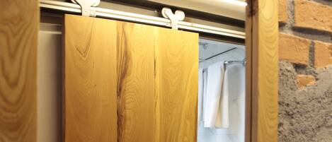 A wooden-framed mirror with a light fixture above it, reflecting a bathroom with a white tiled wall and a towel hanging on a rack.