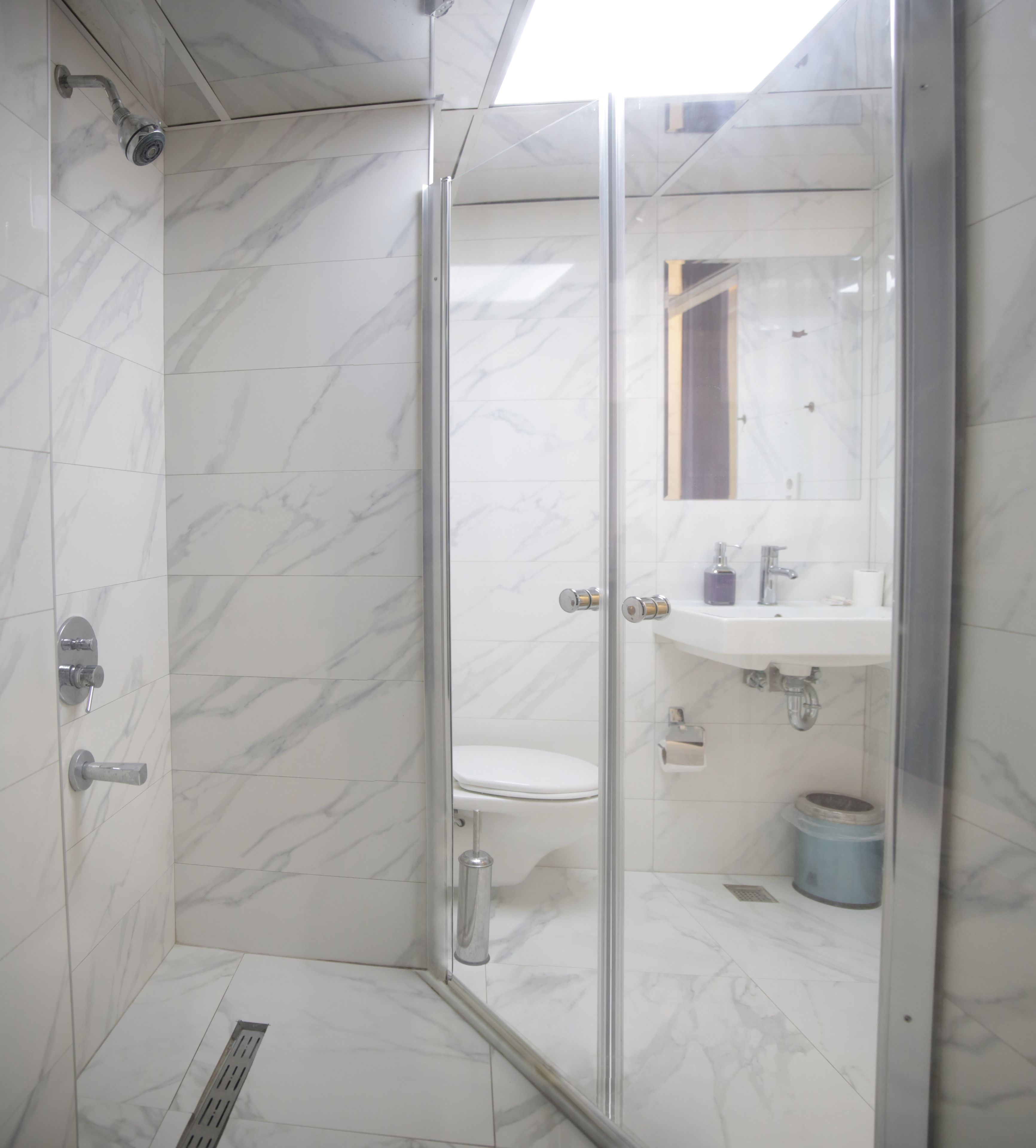 A bathroom with a glass-enclosed shower, a toilet, and a sink with a mirror above it.
