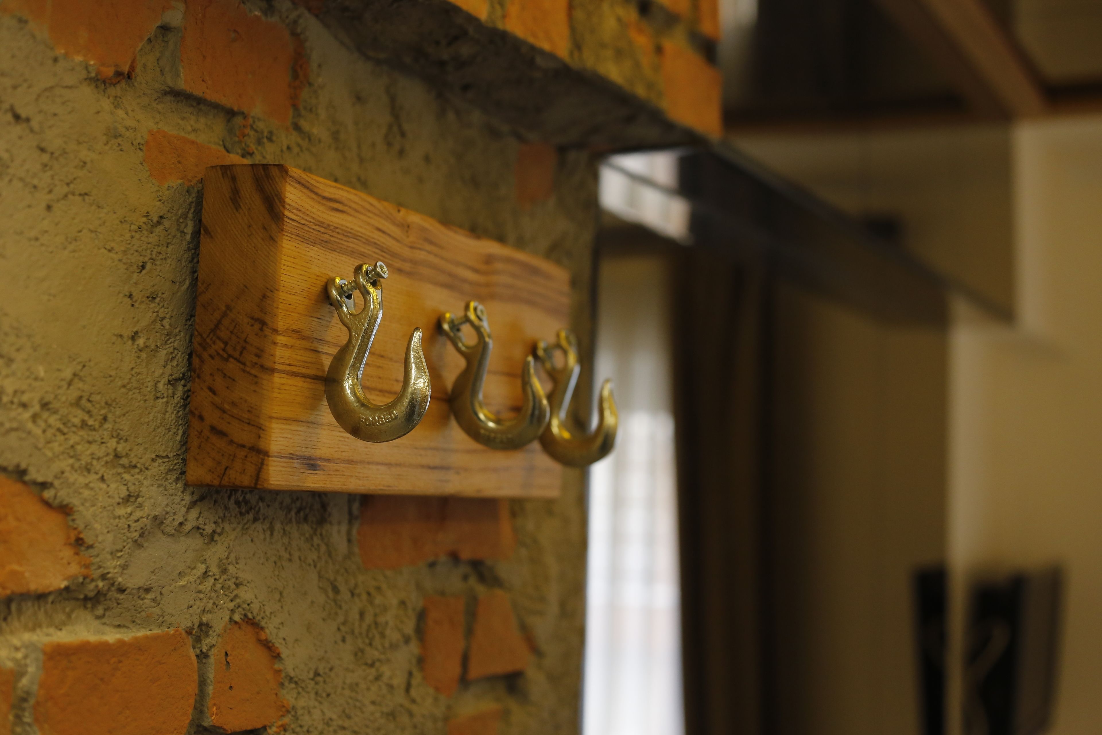 A wooden plaque with three brass door knockers on a brick wall.