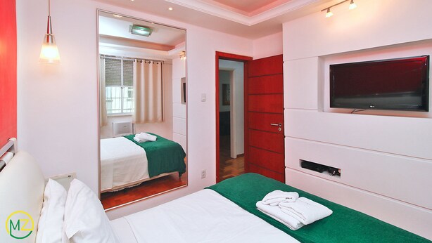 Une chambre d’hôtel avec un lit, un miroir, une télévision et une porte rouge.