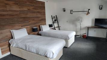 Moderni hotellihuone, jossa on kaksi sänkyä, puusta tehty koristeellinen seinä, työpöytä, jossa on televisio, ja kattotuuletin.