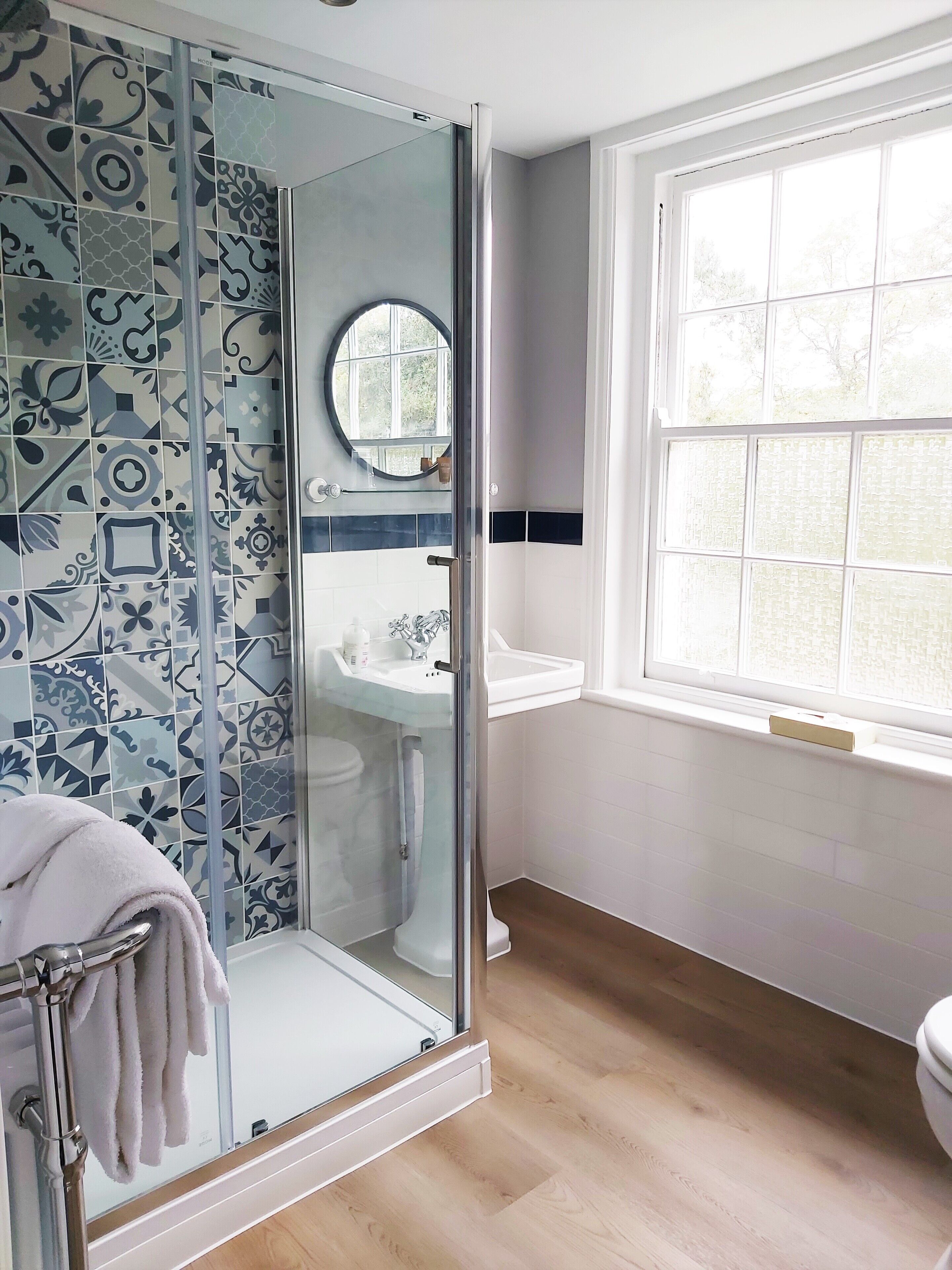 A bathroom with a glass-enclosed shower, a sink, a toilet, and a window with a view of trees.