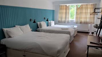 A hotel room with two beds, a desk, a chair, a ceiling fan, and a window with curtains.