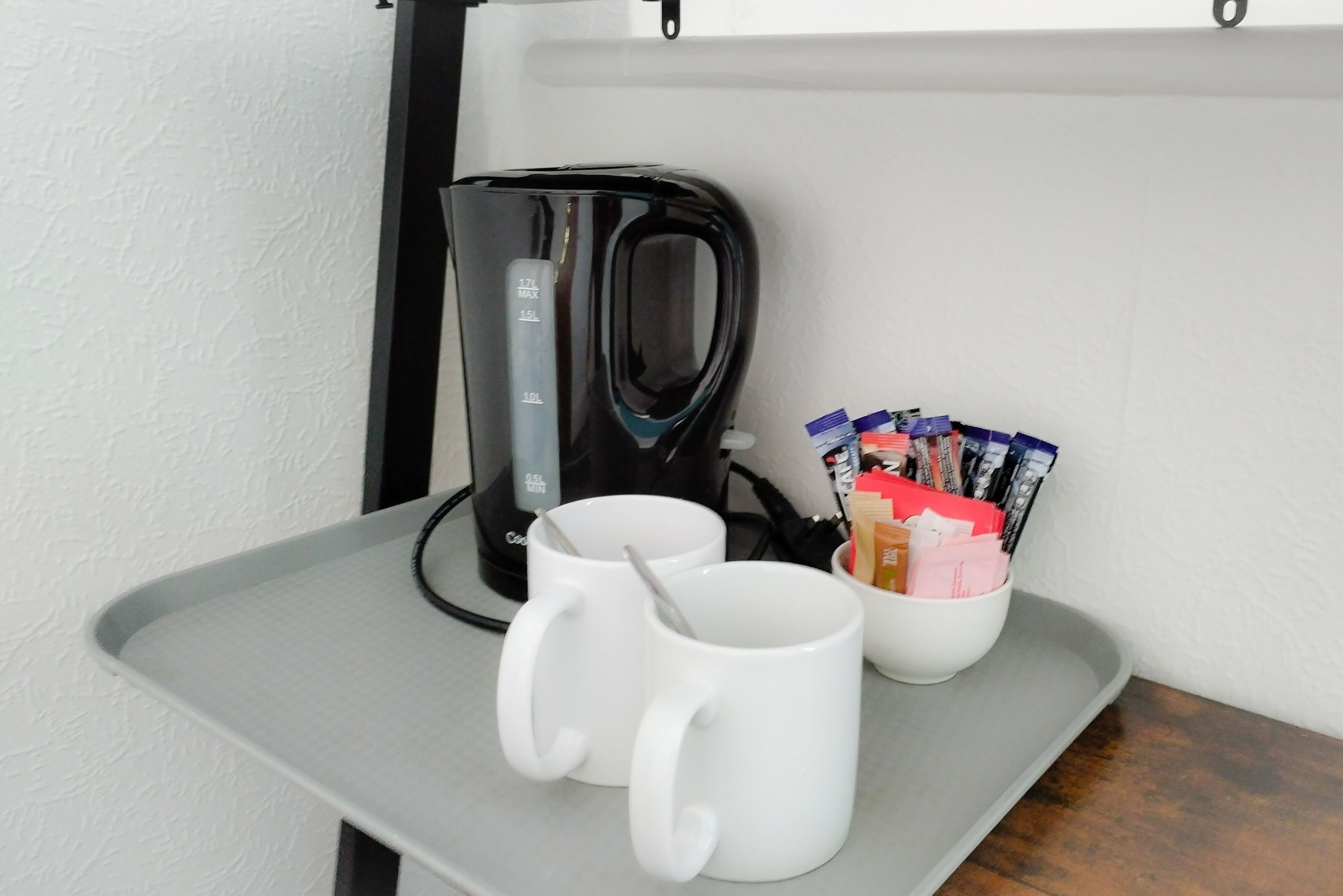 Una cafetera, dos tazas blancas y una cesta con bolígrafos y cuadernos sobre una bandeja.